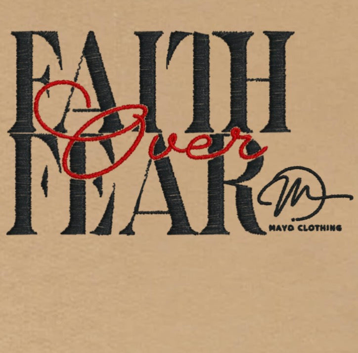 Embroidered text 'Faith Over Fear' with a signature on a sand background